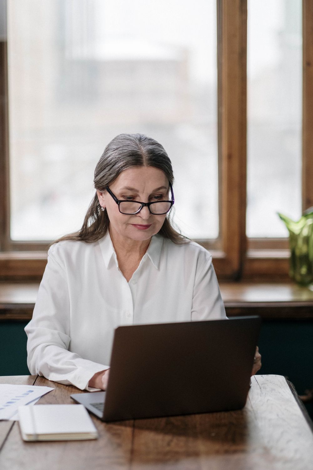 Eine ältere Frau mit Brille arbeitet konzentriert an einem Laptop.